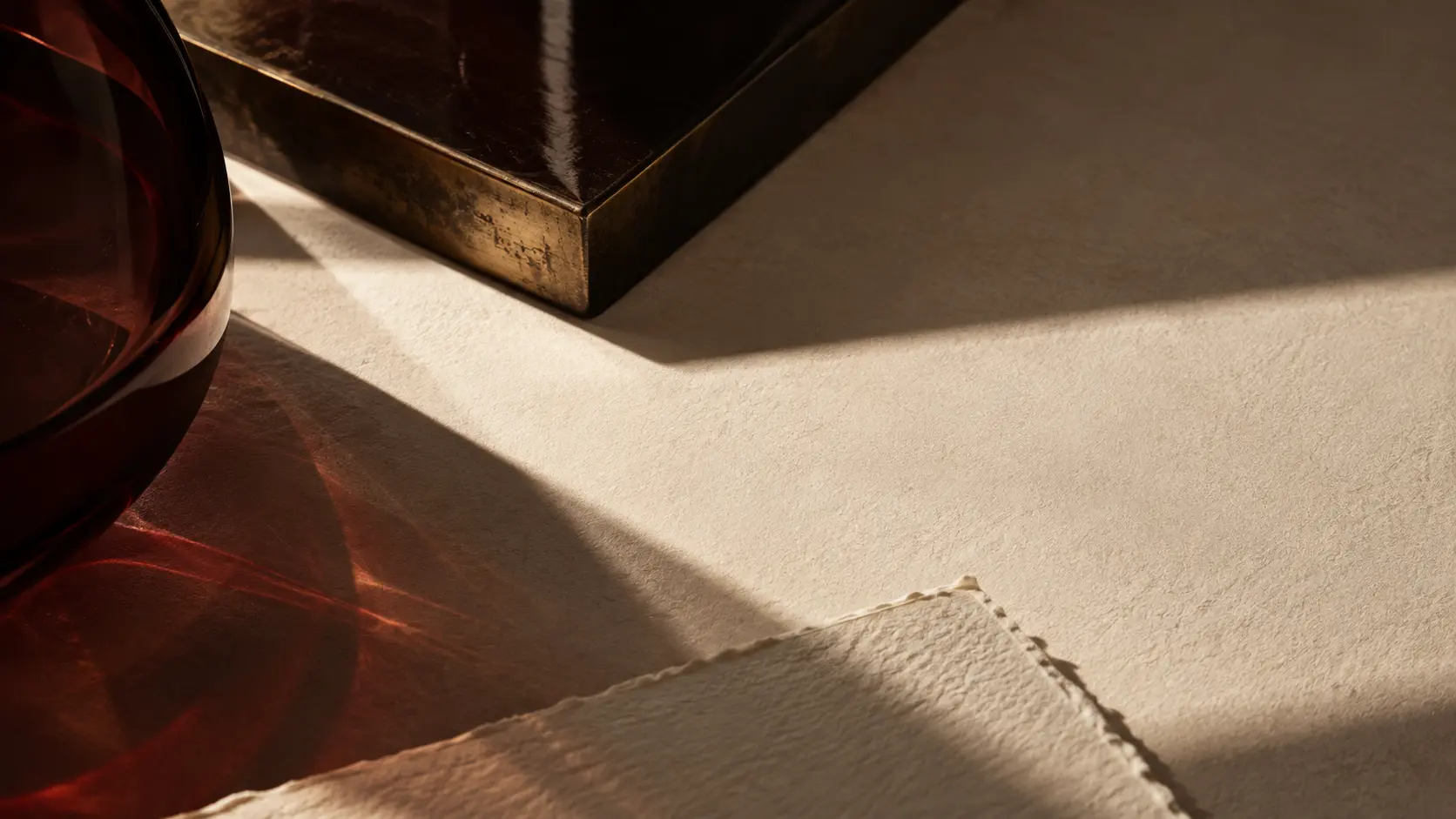 Oxblood glass, aged brass and textured cream paper arranged in directional light.